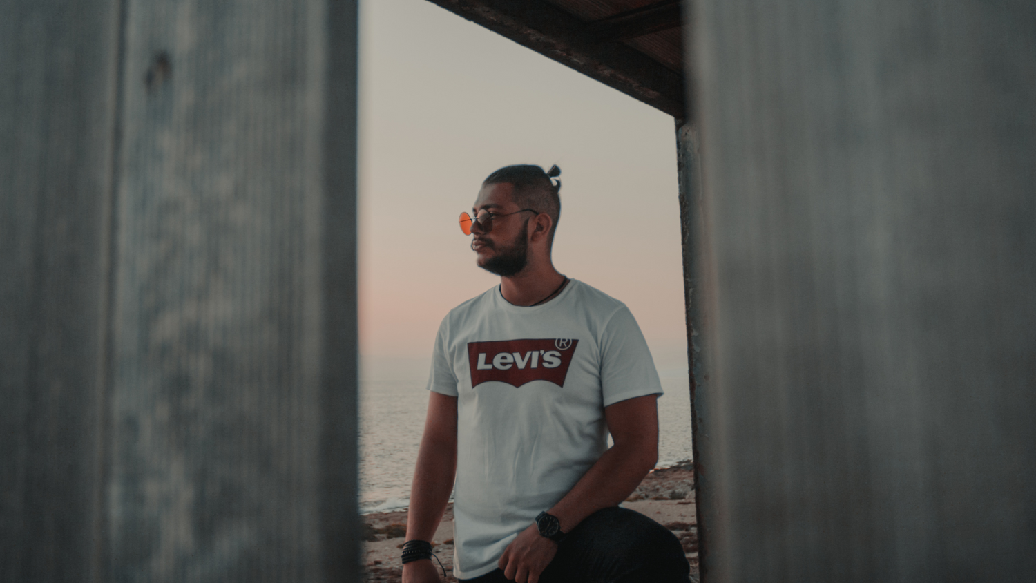 A portrait photo of a male model wearing a black sunglass with printed shirt on a dark background for Blue Specttica sunglass collection page